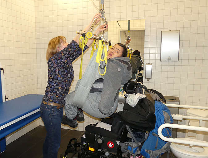 Schwebend mit Hilfe des Lifters vom Rollstuhl auf die Liege. Natascha Cid und Sabine Pose zeigen die Funktionsweise der »Toilette für alle«.<br />Foto: © Mara Sander