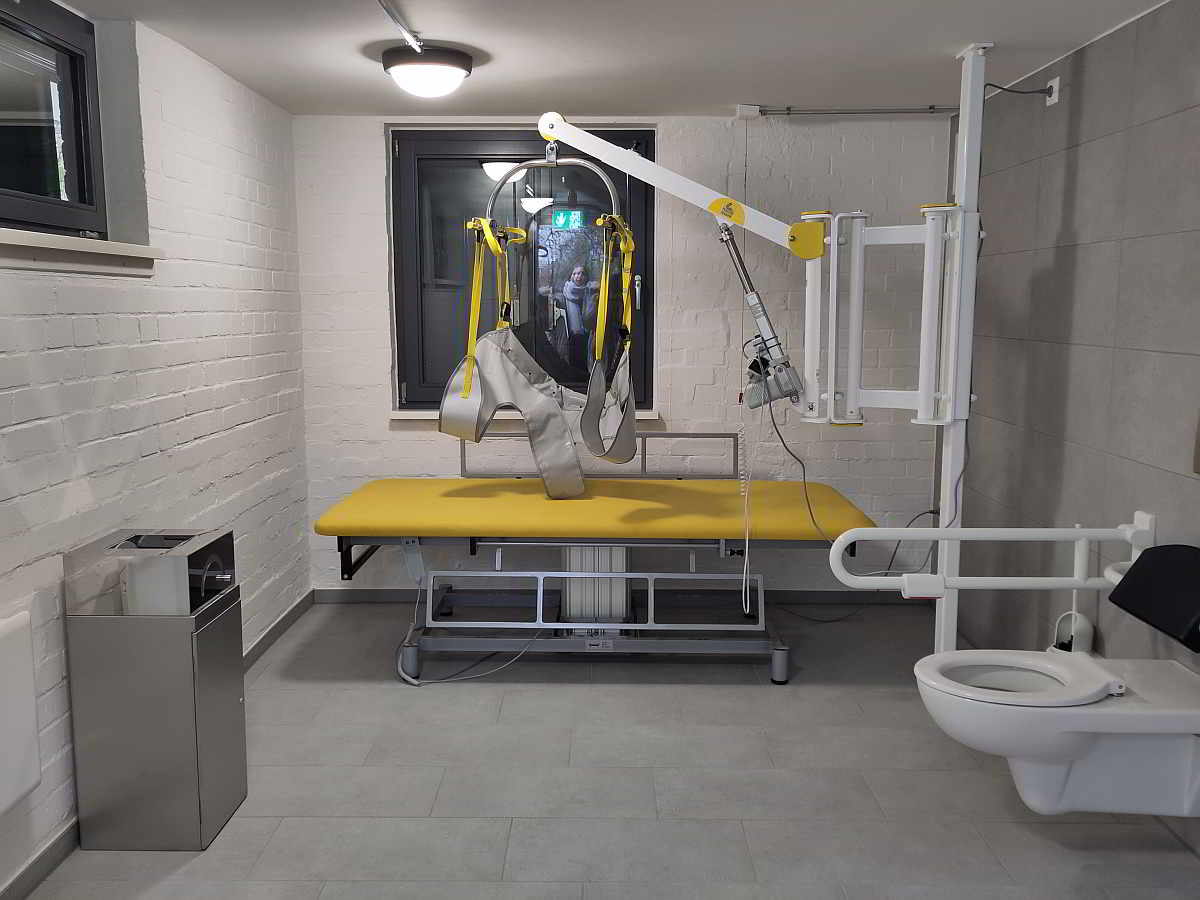 Die rund 12 qm große Rollstuhl-Toilette ist zusätzlich ausgestattet mit einer höhenverstellbaren frei stehenden Pflegeliege für Erwachsene, Wandlifter und luftdichtem Windeleimer. Die „Toilette für alle“ ist mit Euro-Schlüssel 24/7 zugänglich.