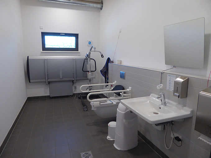 Die geräumige »Toilette für alle« im „Haus am See“ ist mit dem Euro-Schlüssel zugänglich und ausgestattet mit einer höhenverstellbaren Wandklappliege, einem mobilen Patientenlifter sowie einem luftdicht verschließbaren Windeleimer