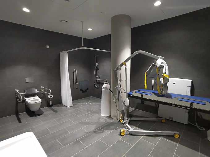 Die rund 16 qm große Rollstuhltoilette einschließlich Dusche im neuen Landratsamt (Raum E0-05-102) ist zusätzlich mit einer höhenverstellbaren Wandklappliege für Erwachsene (mit abklappbarem Seitengitter), einem mobilen Lifter (Hebetuch vorhanden) sowie einem luftdichten Windeleimer ausgestattet. Sie ist während der Öffnungszeiten zugänglich.