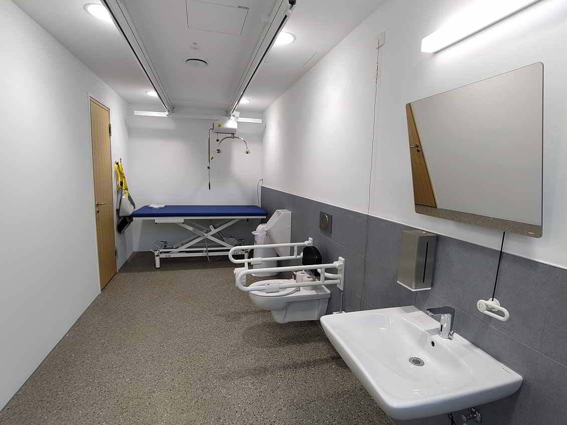 Die rund 13 qm große barrierefreie „Toilette für alle“ ist sehr geräumig und ausgestattet mit einer frei stehenden höhenverstellbaren Pflegeliege für Erwachsene, einem Deckenlifter (Hebetuch vorhanden) und einem luftdichten Windeleimer